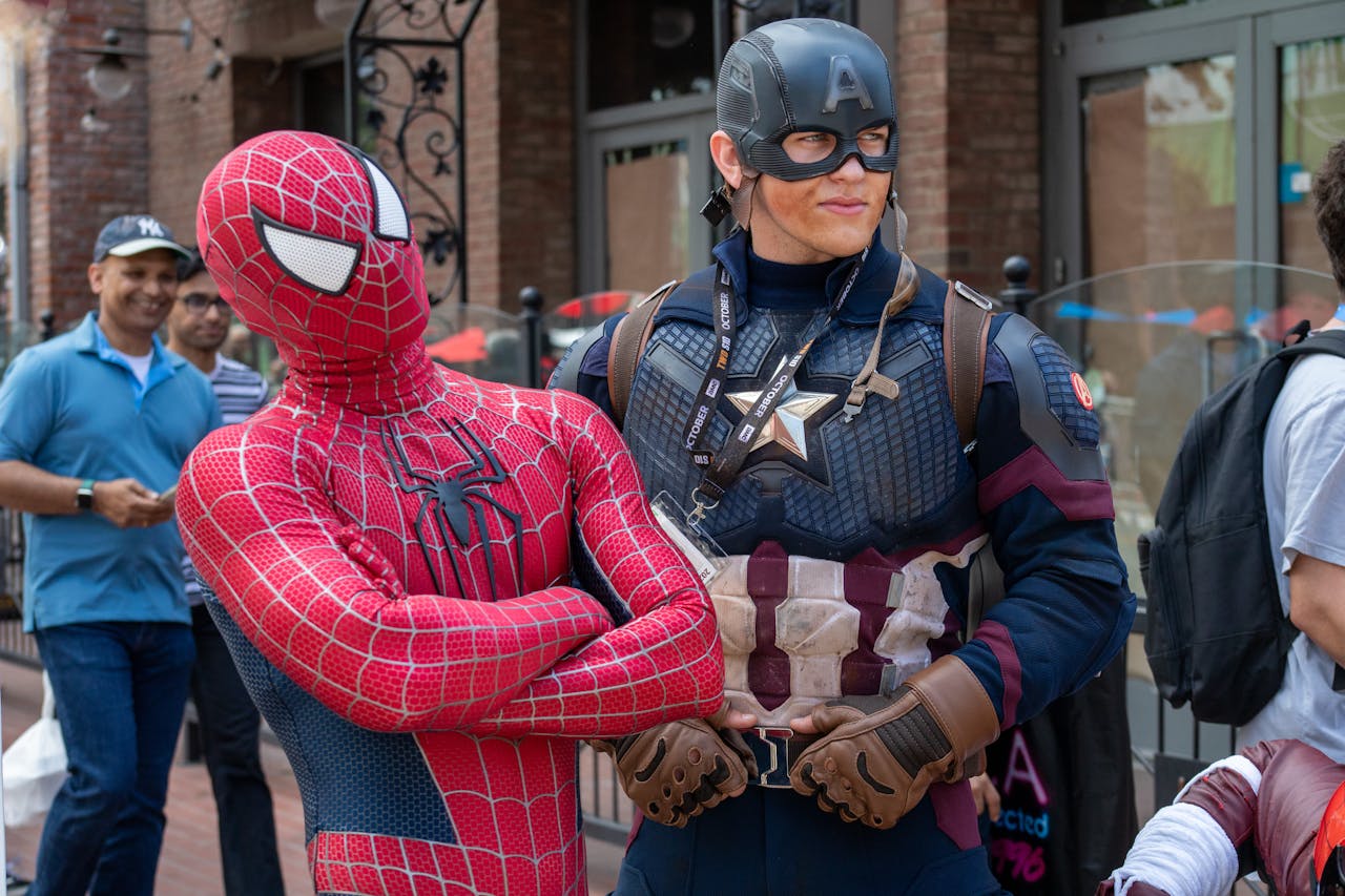 Spider-Man and Captain America cosplayers pose in a lively street scene with onlookers.